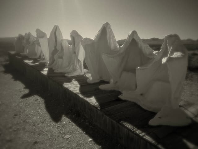 Row of pointed grave markers casting long shadows in a sepia-toned cemetery scene