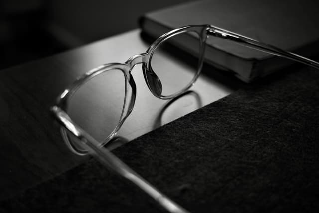 A pair of eyeglasses resting on a table next to a closed book, captured in black and white