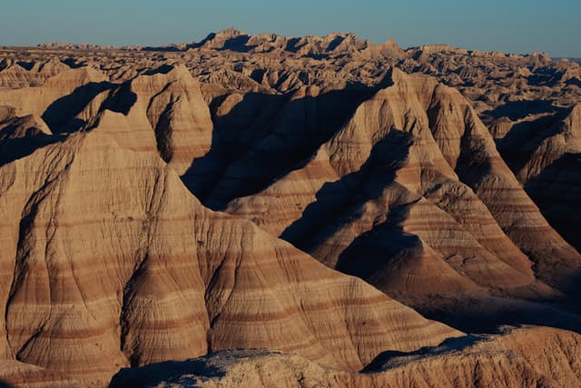 Layered badlands with striated sedimentary ridges and rugged, eroded cliffs in warm evening light
