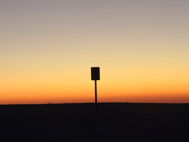Silhouette of a lone signpost against a gradient sunset sky