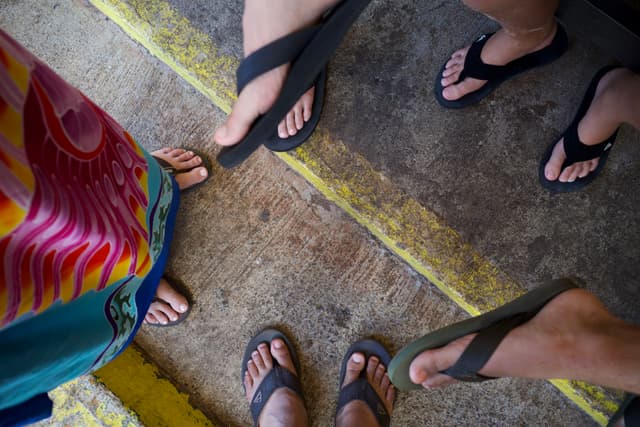 Four people wearing flip-flops standing on a concrete surface with yellow lines
