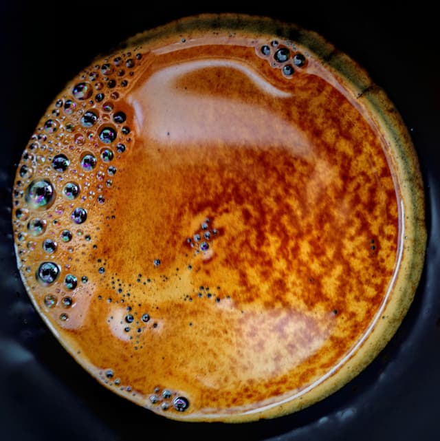 A close-up of a cup of espresso with a rich crema and bubbles on the surface