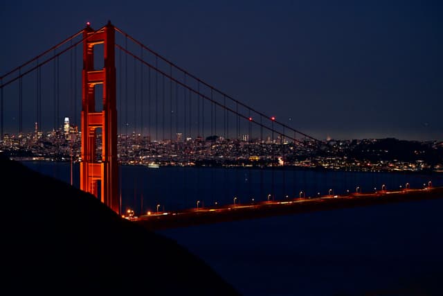 The Golden Gate Bridge illuminated at night with a city skyline in the background