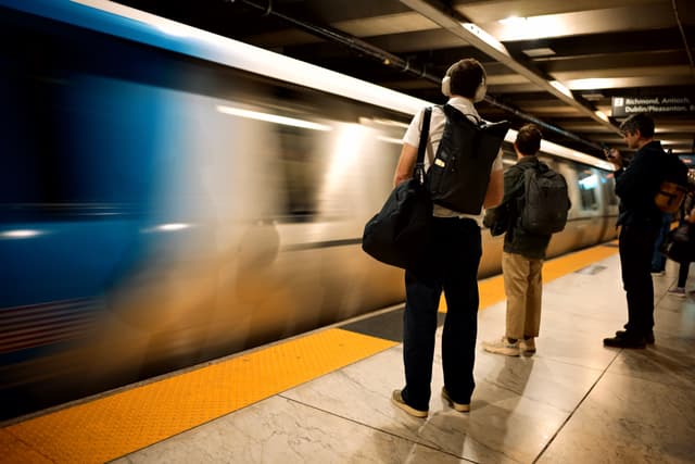 A subway platform with people waiting as a train speeds by, creating a motion blur effect