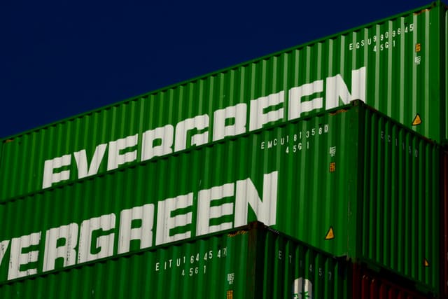 Green shipping containers stacked against a clear blue sky, with the word EVERGREEN prominently displayed in white letters