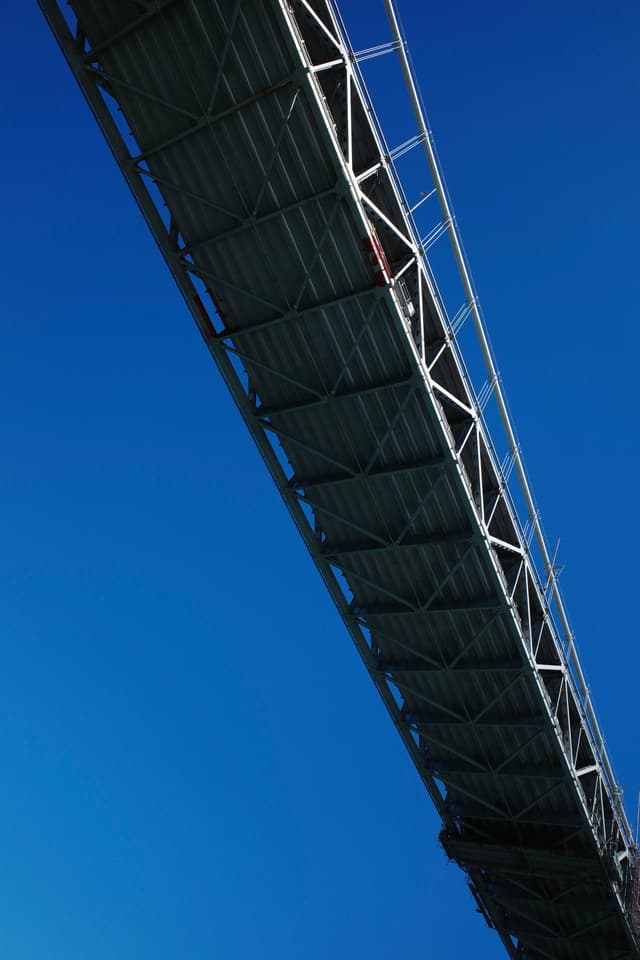 A bridge with a metal framework against a clear blue sky, viewed from below