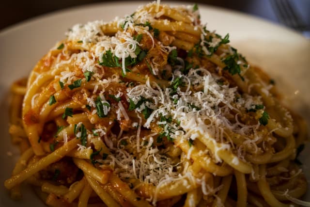A plate of spaghetti topped with grated cheese and chopped herbs