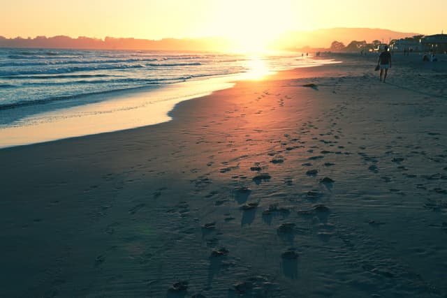 A serene beach at sunset with footprints in the sand, gentle waves, and a warm, glowing horizon