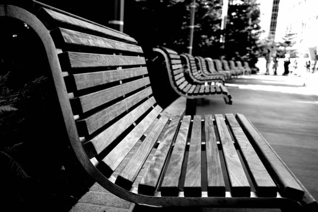 A row of modern, wooden slatted benches in a black and white urban setting
