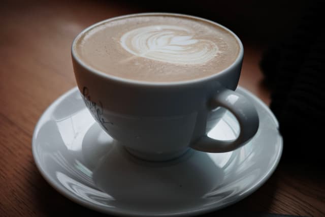 A cup of coffee with latte art on a white saucer, placed on a wooden surface