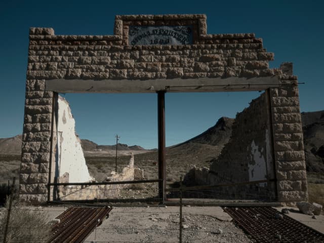 Stone doorway ruins with a wooden crossbeam in an abandoned desert settlement under a dark blue sky