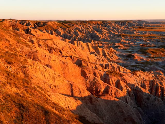 Sunlit badlands with layered, eroded cliffs glowing orange at sunset, stretching across a vast arid landscape