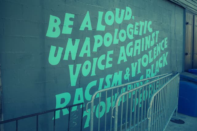 A mural with bold text encourages being a loud, unapologetic voice against racism and violence towards Black people