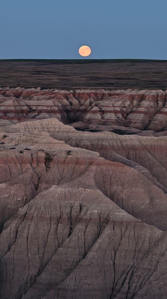 Full moon above a rugged, layered badlands landscape at dusk