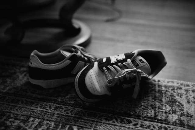 Pair of sneakers resting on a patterned rug with a person lying blurred in the background
