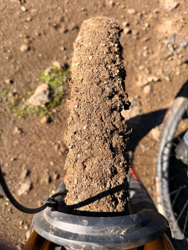 Close-up of a bicycle tire coated in thick dried mud on a rocky dirt trail