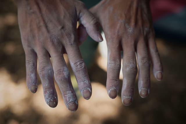 Two hands covered in chalk, likely from rock climbing, with visible wear and dirt