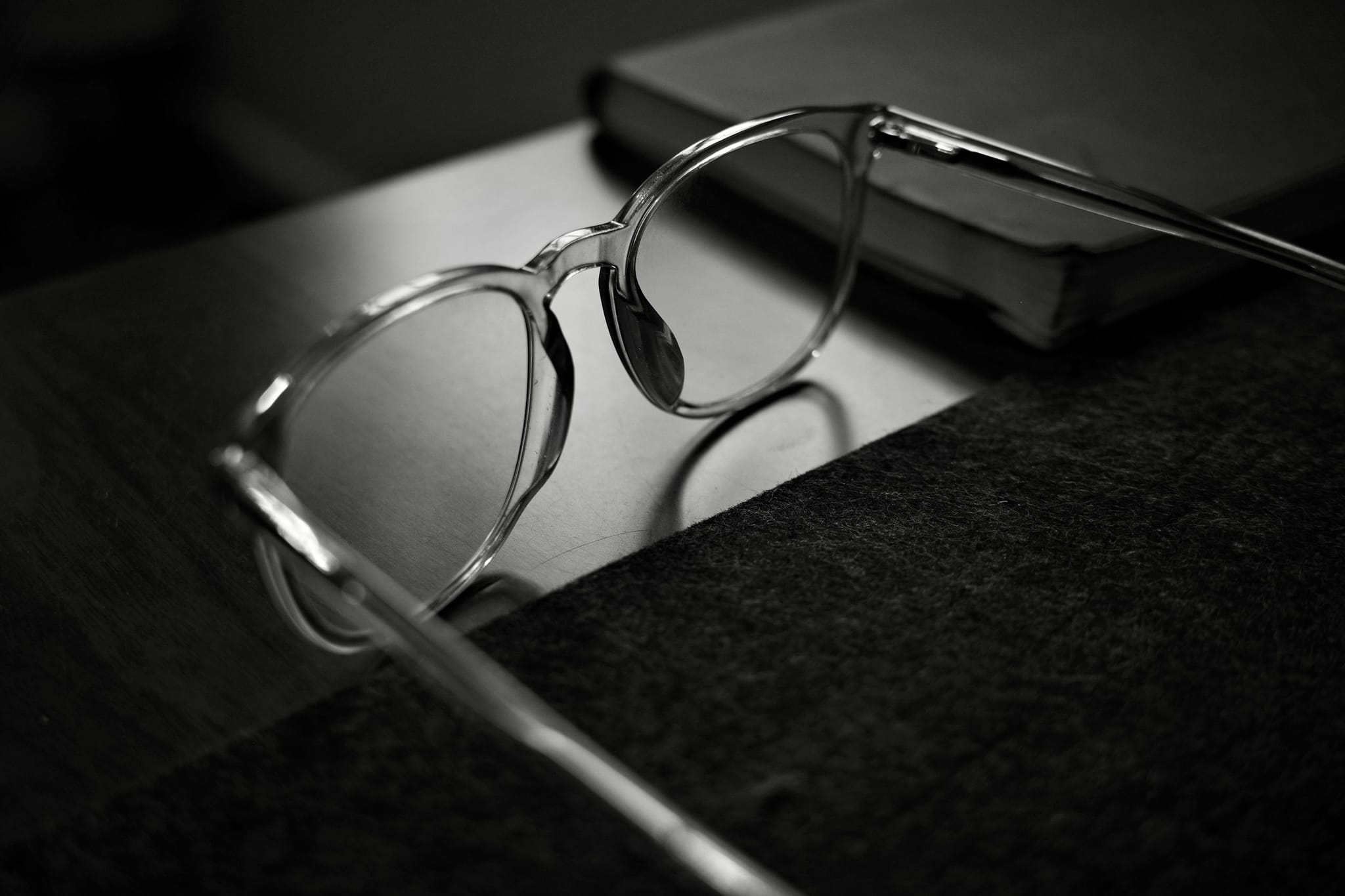 A pair of eyeglasses resting on a table next to a closed book, captured in black and white