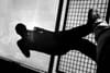 A black and white reflection of a person taking a photo, with their shadow cast on a wet surface next to a grid-like structure