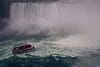 A red-and-white tour boat approaches the misty base of a massive waterfall, likely Niagara Falls