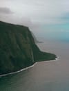Steep green cliffside along the coastline with a waterfall cascading into the sea and a distant horizon