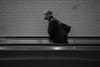 A person walking on a moving walkway in a subway station, captured in black and white