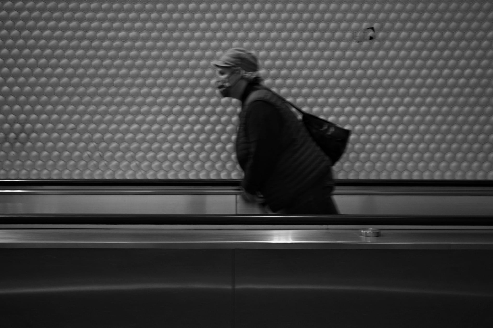 A person walking on a moving walkway in a subway station, captured in black and white