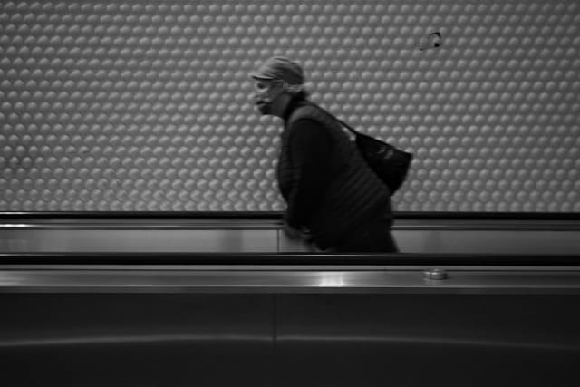 A person walking on a moving walkway in a subway station, captured in black and white