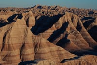 Layered badlands with striated sedimentary ridges and rugged, eroded cliffs in warm evening light