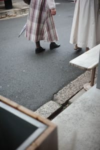 Two people in long skirts walking on a street, one holding an umbrella
