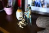 A small collection of decorative items on a wooden surface, including a colorful giraffe figurine, a golden rabbit, and a textured vase, with a framed photo in the background