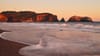 A serene coastal scene at sunset with gentle waves washing onto a sandy beach, rocky cliffs in the background, and a warm, golden glow illuminating the landscape