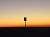 Silhouette of a lone signpost against a gradient sunset sky