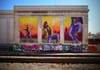 A vibrant mural on a building wall features three panels depicting dancers in dynamic poses against a colorful background. The word groove is prominently displayed above the central figure. Below the mural, a row of graffiti covers a low wall near train tracks