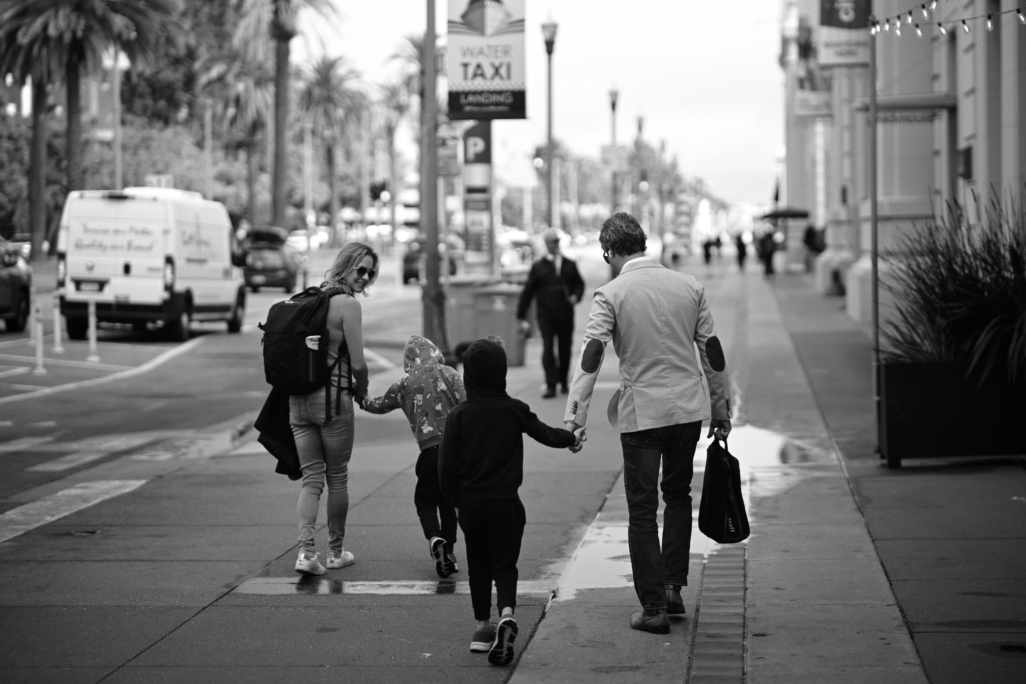 A black and white photo of a family walking down a city sidewalk, with two adults and two children holding hands