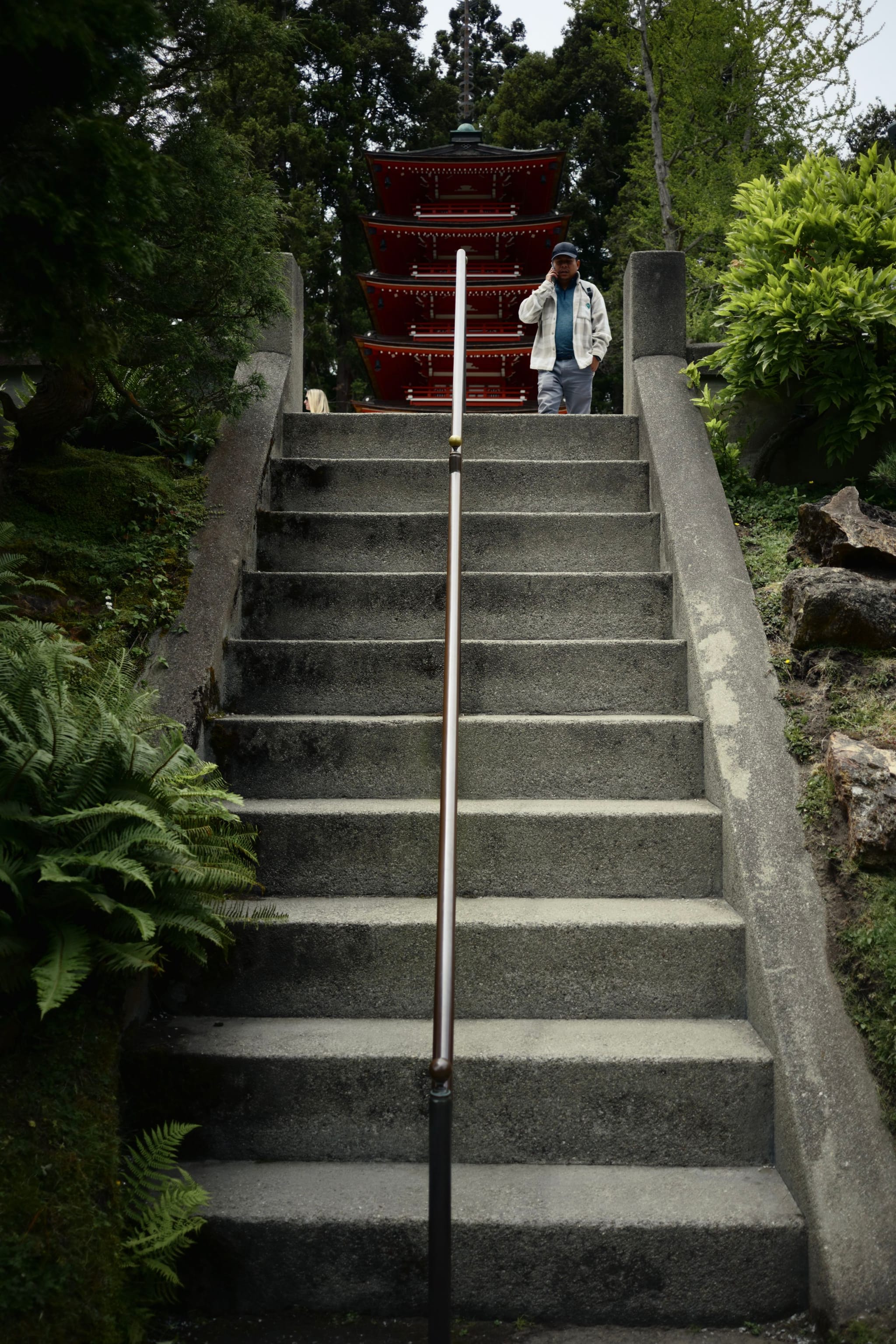 A person walking down a stone staircase with a red pagoda in the background, surrounded by greenery