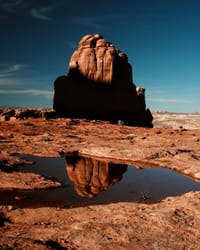Sandstone monolith reflected in a puddle on desert slickrock