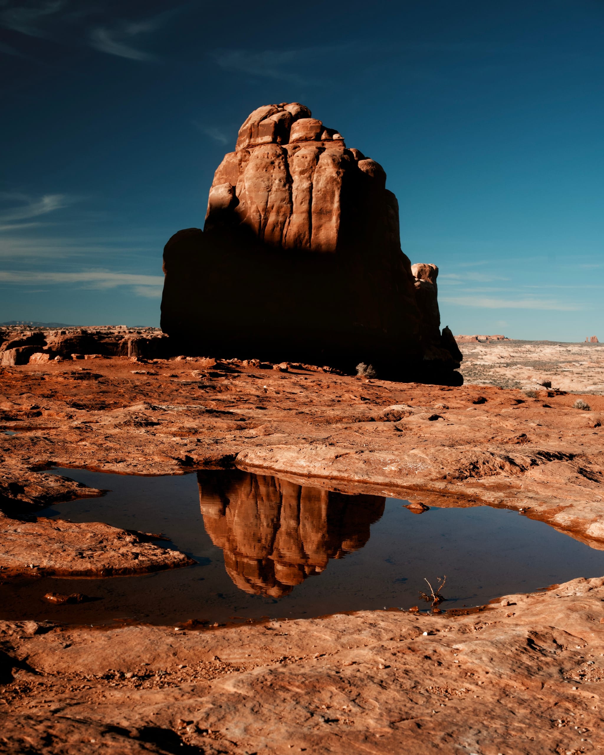 Sandstone monolith reflected in a puddle on desert slickrock