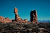 Balanced rock formation and sandstone spire in a desert landscape with distant snowcapped mountains under a clear blue sky
