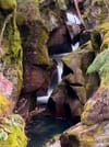 A small waterfall threads through a narrow, moss-covered rocky gorge, pooling in a blue basin below