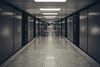 A long, empty corridor with a polished floor, flanked by dark walls and illuminated by overhead fluorescent lights
