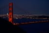 The Golden Gate Bridge illuminated at night with a city skyline in the background