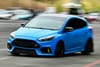 A blue sports car driving on a road with a blurred background, indicating motion