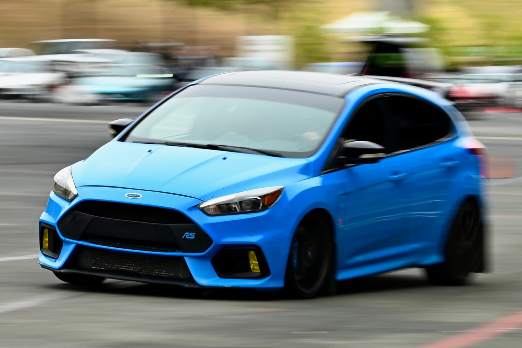 A blue sports car driving on a road with a blurred background, indicating motion
