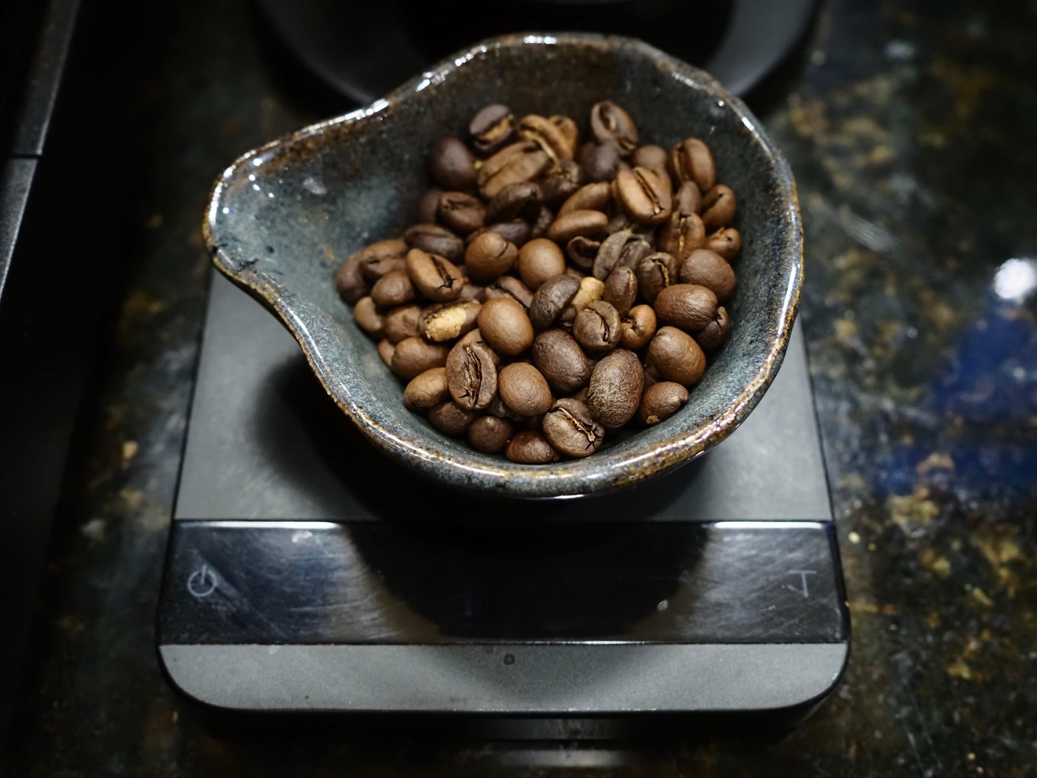 Close-up of roasted coffee beans in a small ceramic bowl on a digital kitchen scale
