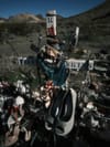 Roadside memorial cross surrounded by flowers, candles, and ski gear in a desert roadside setting