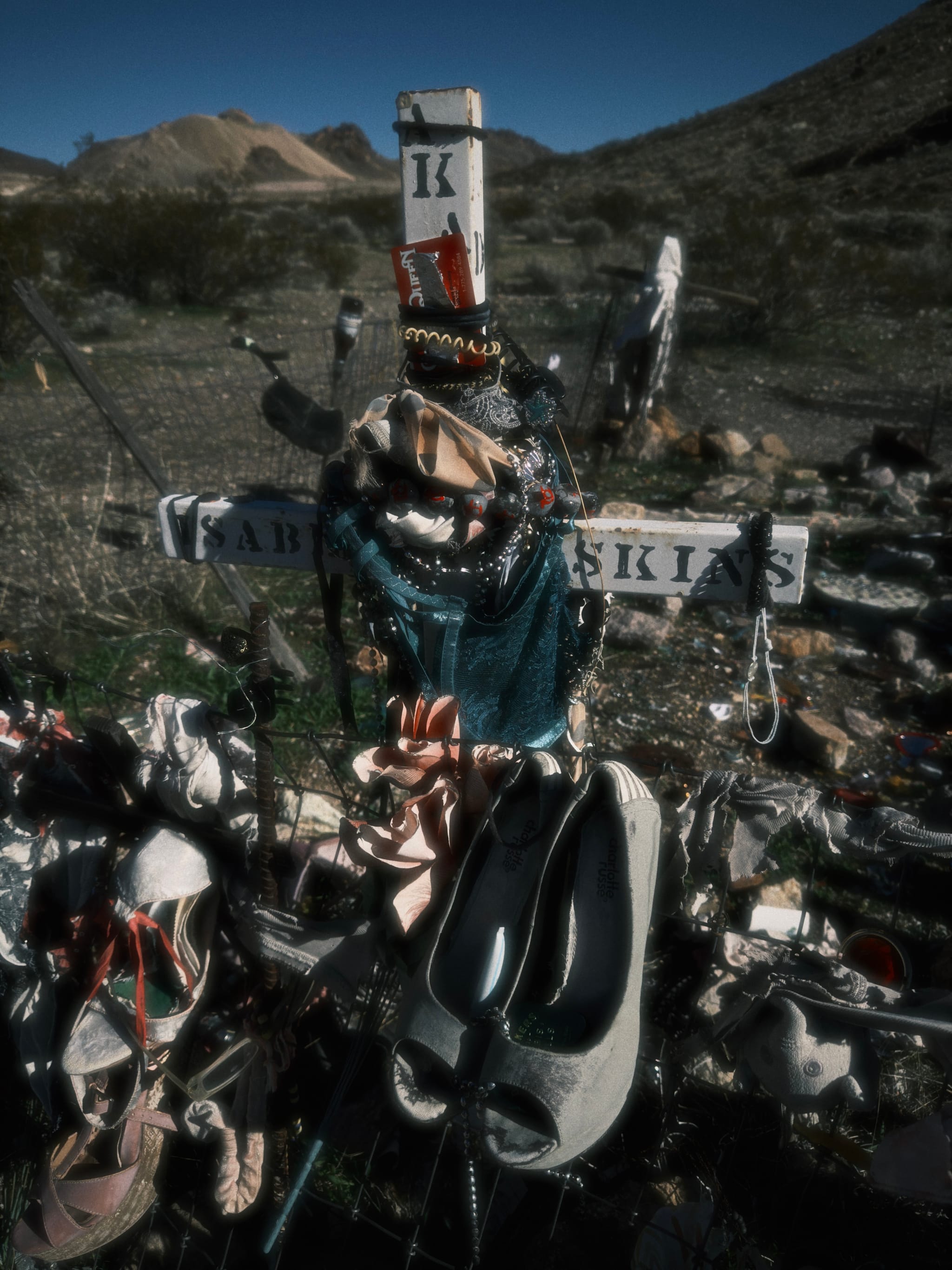 Roadside memorial cross surrounded by flowers, candles, and ski gear in a desert roadside setting
