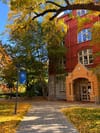 Red-brick building with an arched doorway, autumn foliage, and a paved walkway along a leaf-strewn path