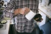 A person in a plaid shirt pouring milk from a white pitcher into a cup of coffee