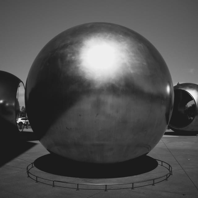 A large, reflective metal sphere on a concrete surface with a clear sky in the background